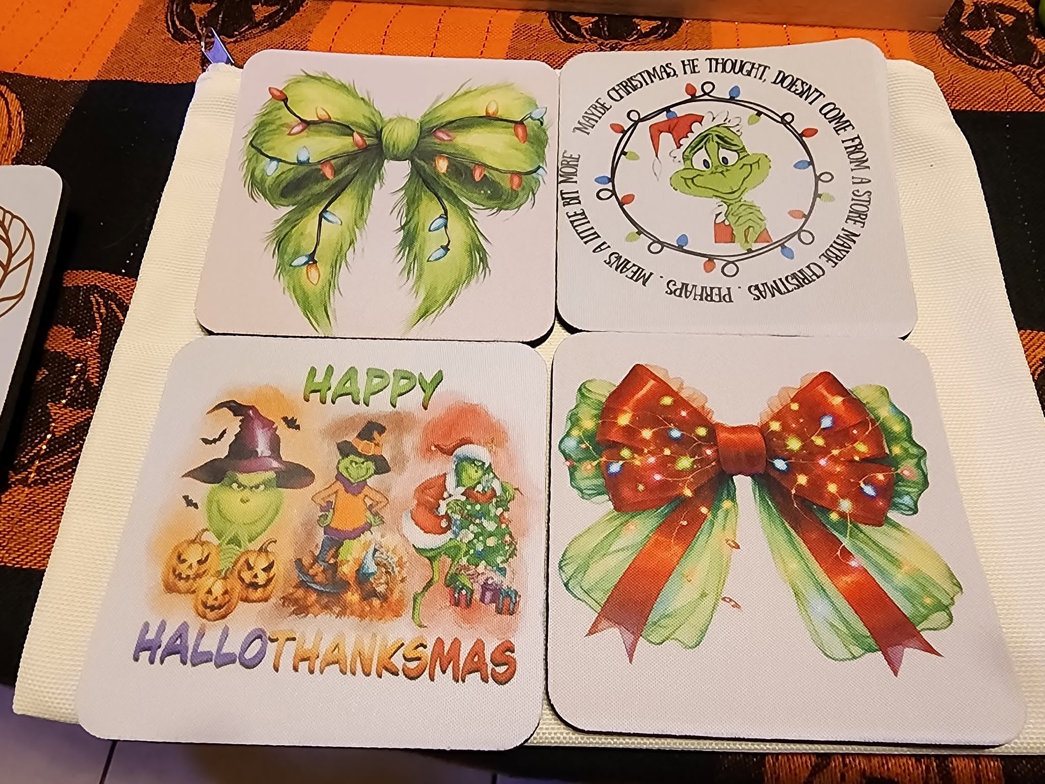 Four square Christmas-themed coasters feature festive illustrations including a green Grinch-like character, holiday bows with lights, pumpkins, and text such as 'HALLOWEEN Thanksgiving' and 'HAPPY CHRISTMAS.